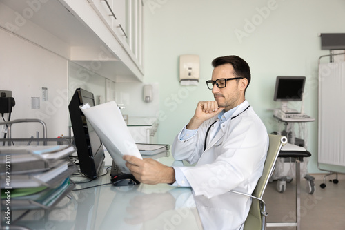 Serious professional ultrasonographer doctor reviewing ultrasound scan result, reading medical records, history, examination report, thinking on diagnosis at workplace in sonography room