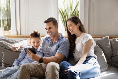 Couple of cheerful parents and little son kid watching funny online content on mobile phone, using digital technology for funny leisure, entertainment, Internet communication