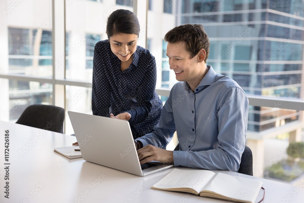 Diverse office friends meeting at laptop, testing professional application for job, smiling. Indian manager woman giving corporate help, showing online content to male colleague, pointing at screen Diverse office friends meeting at laptop, testing professional application for job, smiling. Indian manager woman giving corporate help, showing online content to male colleague, pointing at screen
