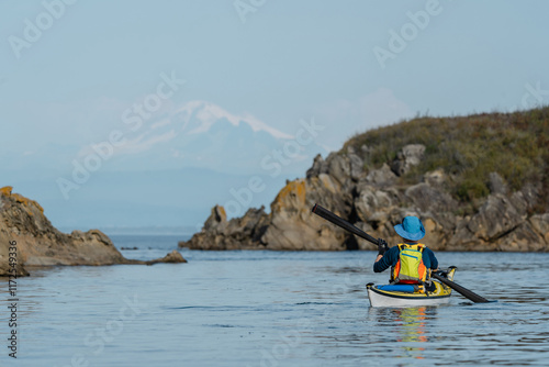 Woman kayaking along Sucia Island in the San Juan Islands in the Pacific Northwest in Washington with Mt Baker in background