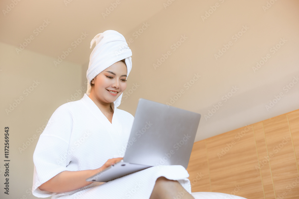young woman chatting on a video call to her friend using laptop while sitting on double bed in bedroom. young woman chatting on a video call to her friend using laptop while sitting on double bed in bedroom.