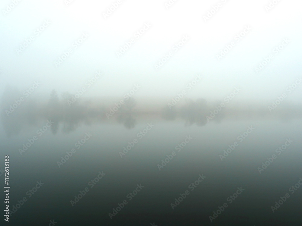 Fototapeta premium Mining pond in the Harz in the fog. A mystical mining pond in the Harz. Fog, reflections, and horizons in winter create an enigmatic atmosphere, perfect for diverse themes.
