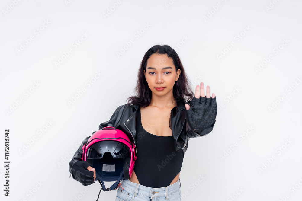 Portrait of a young female motorcycle rider in a black leather jacket and pink helmet, advising to be cautious. Giving stop gesture with hand. Isolated on a white background. Portrait of a young female motorcycle rider in a black leather jacket and pink helmet, advising to be cautious. Giving stop gesture with hand. Isolated on a white background.