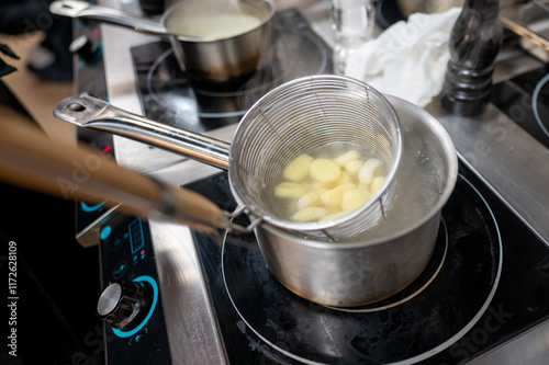 A close-up of a stainless steel pot on a modern stove, with a colander holding cooked dumplings being submerged in boiling water. Steam rises, creating a cozy kitchen atmosphere. photo