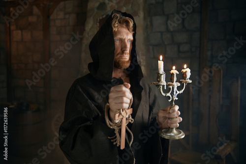 Portrait of hooded monk in medieval costume holding wooden cross and candlestick photo