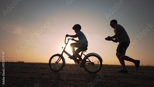 Father's Day. Father teaches son to ride bicycle wearing safety helmet. child learn to ride bicycle in park at sunset. Happy family concept and dream. Active father teaches child to ride bike in park photo