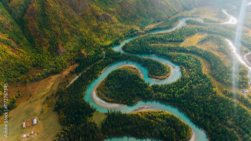 Aerial view of a turquoise river winding through a vibrant green forest. Creating stunning loops and patterns. Nestled within a picturesque mountain valley. Showcasing the beauty of nature's artistry