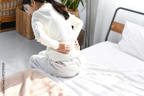 Foto ベッドの上で腰を抑える若い女性の後ろ姿