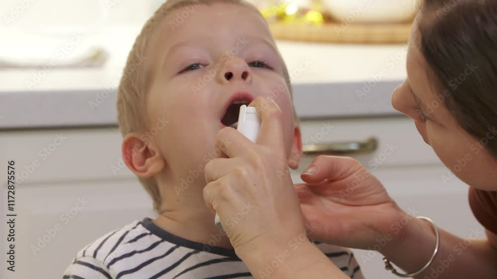 Mother using medical throat spray for little boy at home. Woman spraying aerosol into child's mouth. Mother using medical throat spray for little boy at home. Woman spraying aerosol into child's mouth.