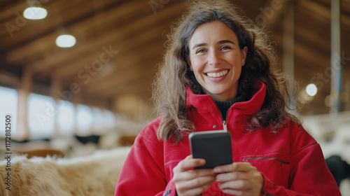 An agricultural worker in a red jacket in a cow barn, smiling as she checks her mobile device, representing a contemporary approach to farm management. female farm worker, dairy fa