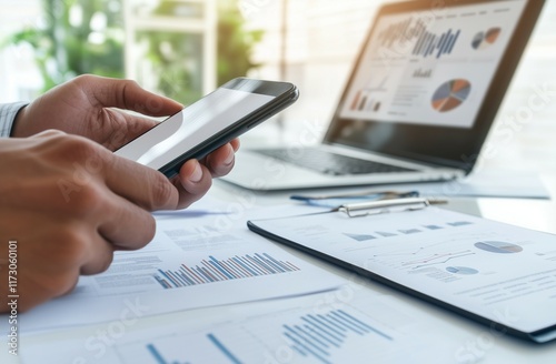 Close-up of a businessman's hand using a white, blank-screen mobile phone with a laptop on the desk in the office. This is a business concept mockup for online social media marketing and digital adver photo