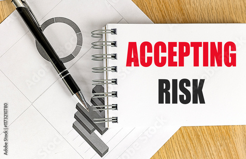 Accepting risk text on a notepad with a black pen and financial charts on a wooden table 