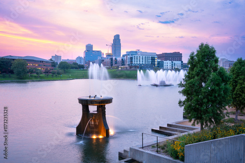 View of Omaha Nebraska skyline at sunset seen from Heartland of America Riverside Park with lake in view.