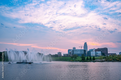 View of Omaha Nebraska skyline at sunset seen from Heartland of America Riverside Park with lake in view.