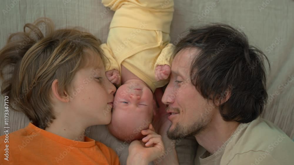 A father and elder brother gently kiss their newborn baby as they all lay together on a bed. A beautiful moment of family love, tenderness, and bonding in a serene and peaceful setting. A father and elder brother gently kiss their newborn baby as they all lay together on a bed. A beautiful moment of family love, tenderness, and bonding in a serene and peaceful setting.