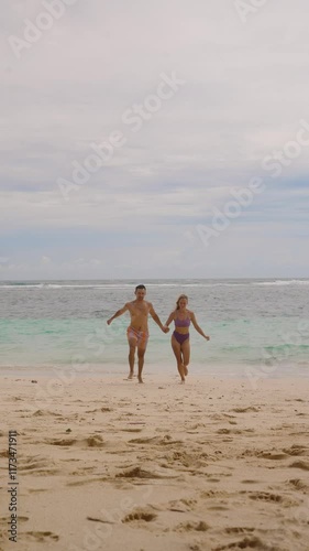 Young couple out of the ocean after swimming, they holding hands, running on sandy beach, enjoying summer trip. Concept of happy memories of honeymoon vacation, date on the beach, travel together photo