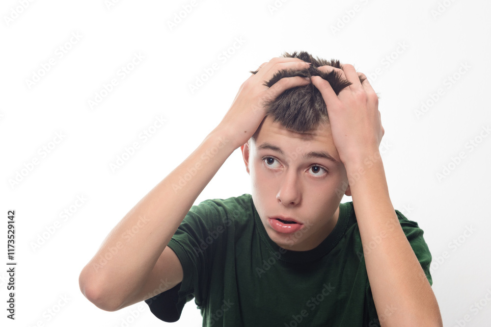 A young man with dark hair looks concerned, his hands on his head. He's wearing a dark green shirt. The background is plain white, focusing attention on his expression. A young man with dark hair looks concerned, his hands on his head. He's wearing a dark green shirt. The background is plain white, focusing attention on his expression.