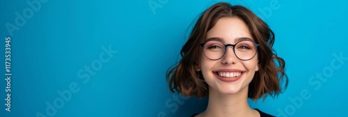 Smiling young woman with glasses against a vibrant blue background. Close-up . Copy space