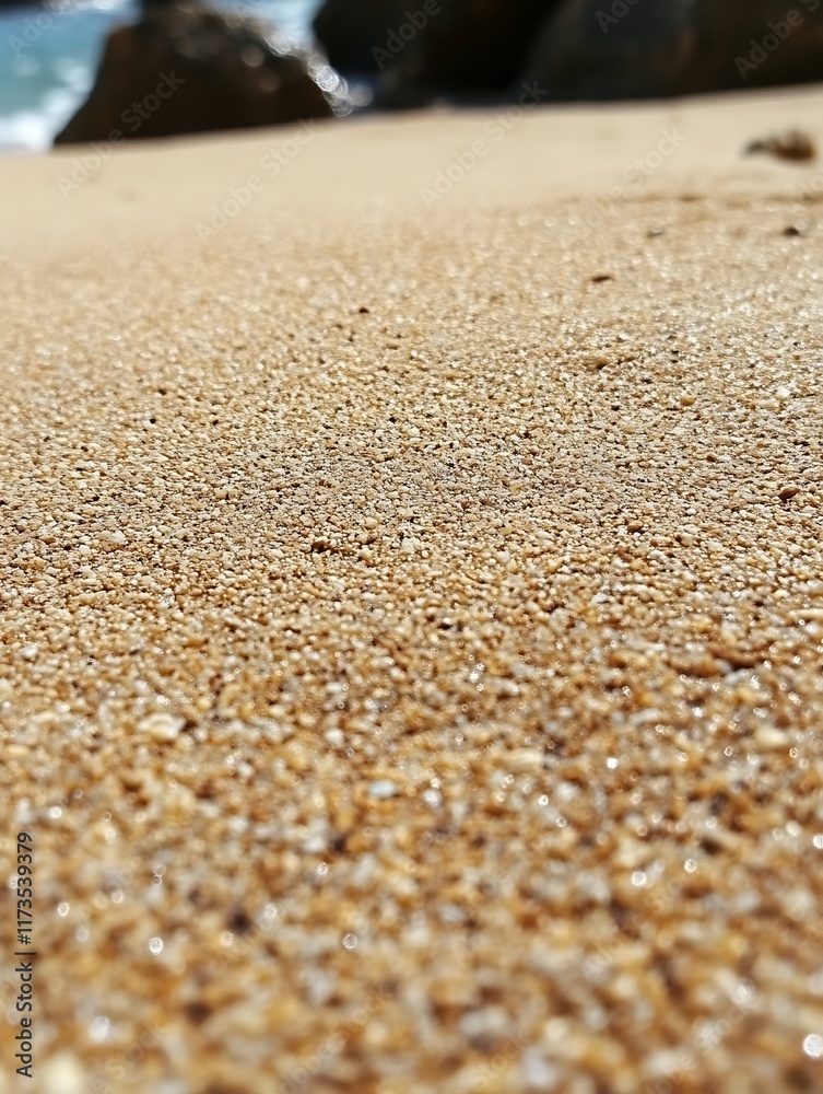 Close-up of sunlit beach sand, shallow depth of field, ocean blurred in background. Close-up of sunlit beach sand, shallow depth of field, ocean blurred in background.