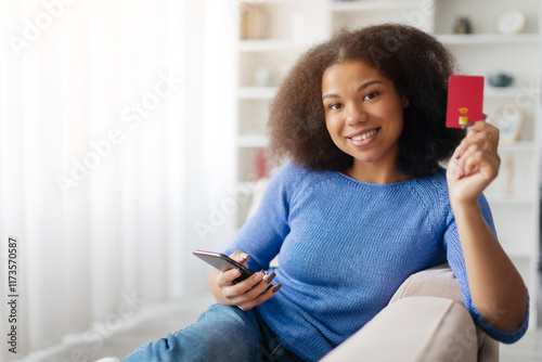 Mobile Banking. Smiling african Female Using Smartphone And Credit Card At Home, Happy Young African American Woman Making Online Payments In App While Sitting On Couch In Living Room. High quality photo