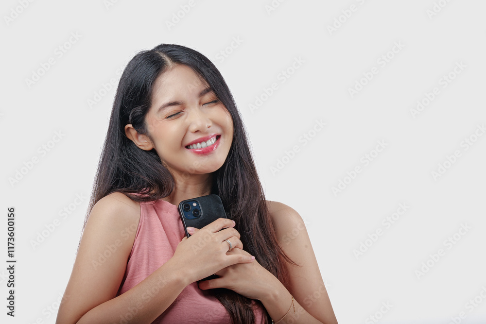 Peaceful young Asian woman is holding a cell phone in her hand and smiling feeling relief. Peaceful young Asian woman is holding a cell phone in her hand and smiling feeling relief.
