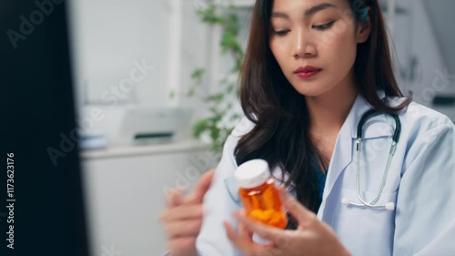 Asian woman Healthcare professional check or review medication details on a computer, with a pill bottle in hand, analyzing prescriptions and details to support patient in the modern hospital room. 