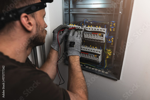 An electrician carefully checks an electrical panel, using a multimeter to measure voltage and ensure safe functionality. Close up.
