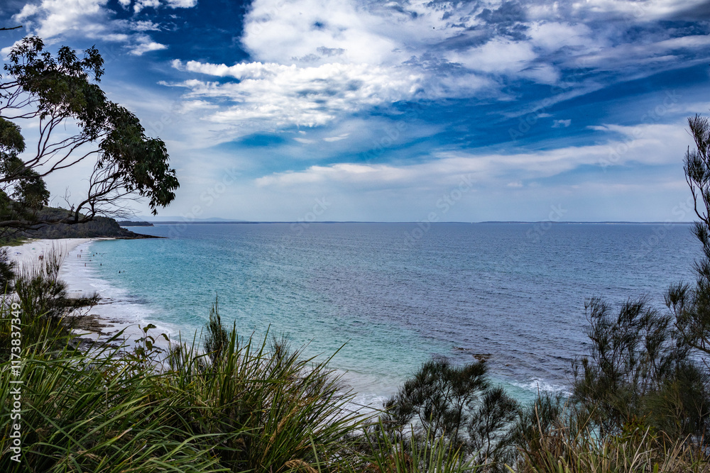 A stunning view of a white sand beach meeting the turquoise ocean under a dramatic blue and white sky. Lush green vegetation frames the scene, creating a vibrant and inviting coastal landscape. A stunning view of a white sand beach meeting the turquoise ocean under a dramatic blue and white sky. Lush green vegetation frames the scene, creating a vibrant and inviting coastal landscape.
