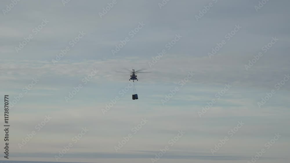 Helicopter carries cargo on a rope. Helicopter transporting two containers over suburban area on a clear afternoon