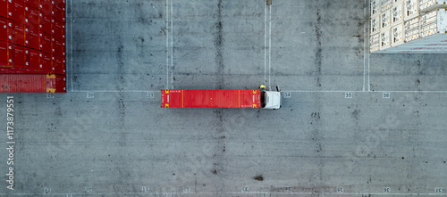 Aerial top-down view of a truck with a red shipping container parked in an industrial freight yard, highlighting logistics and global trade
