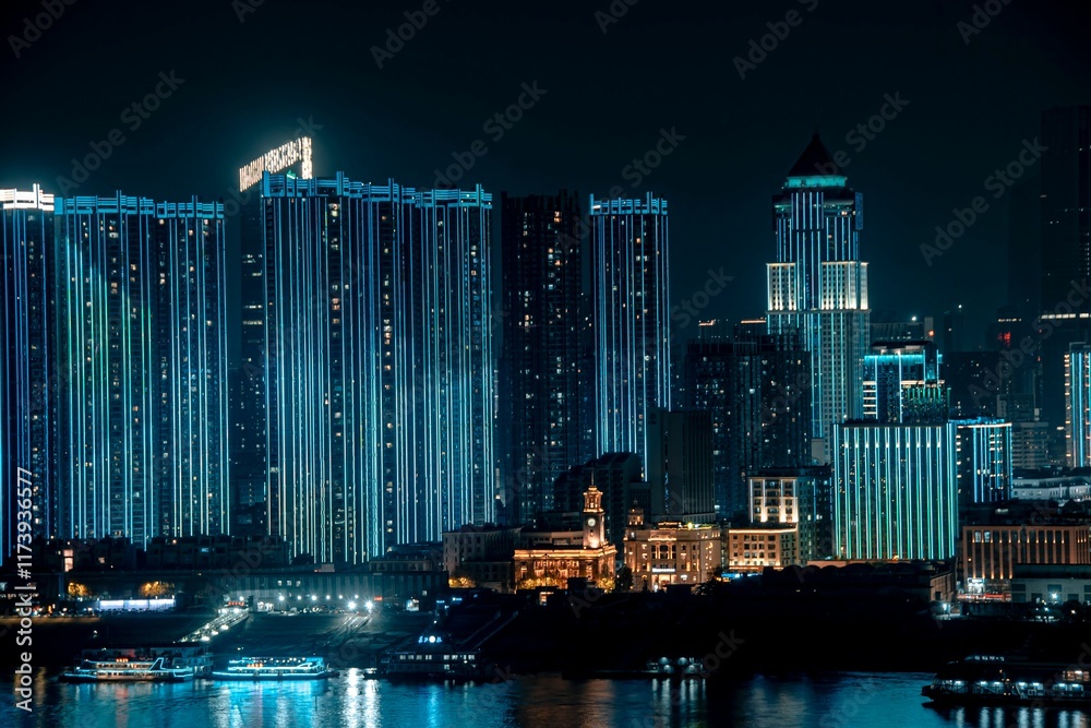Fototapeta premium Illuminated skyscrapers at night reflecting on a river.