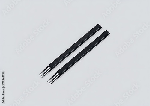 Two black chopsticks with three prongs on light gray background. photo