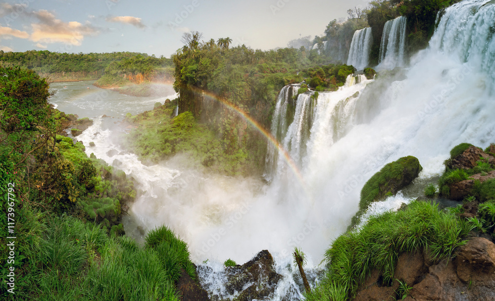 Majestic Iguazu Falls on the Argentine side, with cascading waterfalls surrounded by lush greenery and a misty rainbow arching through the scene