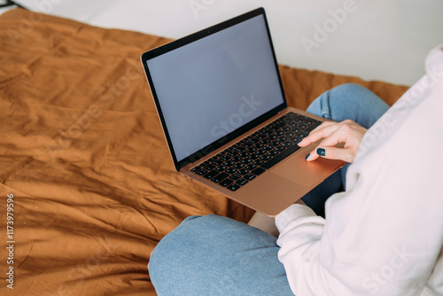 close-up photo of a girl working from home sitting on the bed holding a laptop on her lap