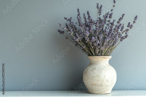 Dried lavender bouquet in a rustic off-white vase against a serene blue-gray wall. photo