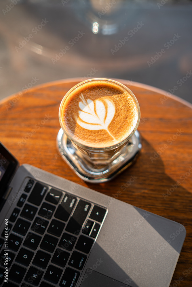 Close-up of Hot coffee latte with latte art milk foam in cup mug and laptop computer on wood desk office desk in coffee shop at the cafe,during business work concept