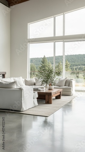 A bright and open living space with concrete flooring, soft gray walls, and expansive windows overlooking a serene landscape