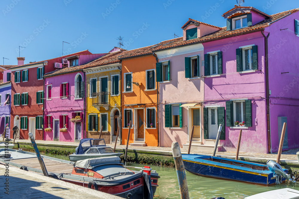 Italy, Burano. Canal and colorful buildings the island is known for. Small boats moored to the sides.