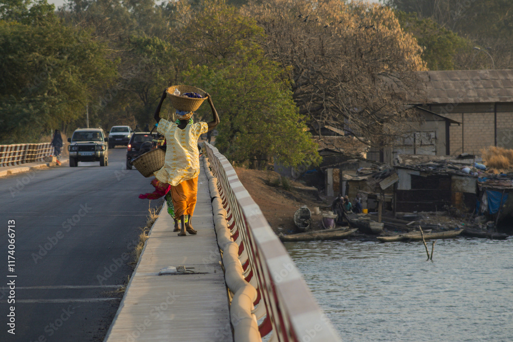 Rear view of a typical african woman walking with basked on head over the bridge over Casamance river in Zuiguinchor, Senegal. Typical african feeling