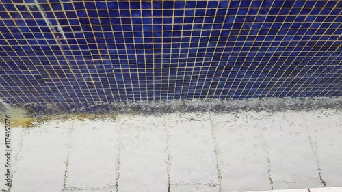 4k video, blue background of the pool texture with small blue mosaic tiles, water from the outdoor pool flows down the wall