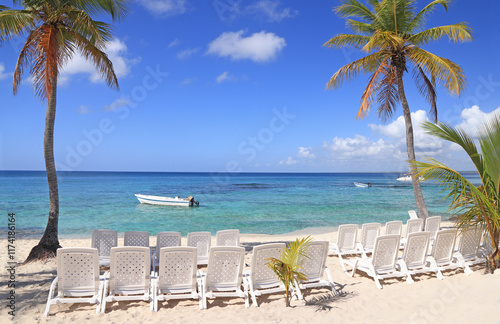 Beautiful beach with white chairs and white sand on the foreground and blue sky on the background on Saona Island, Dominican Republic photo