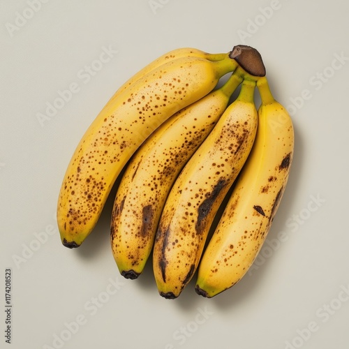 A bunch of four ripe bananas with brown spots on a light grey background. photo