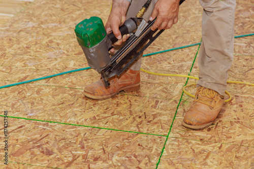 Carpenter worker operates air nail gun to fasten boards as part of flooring installation in construction project.