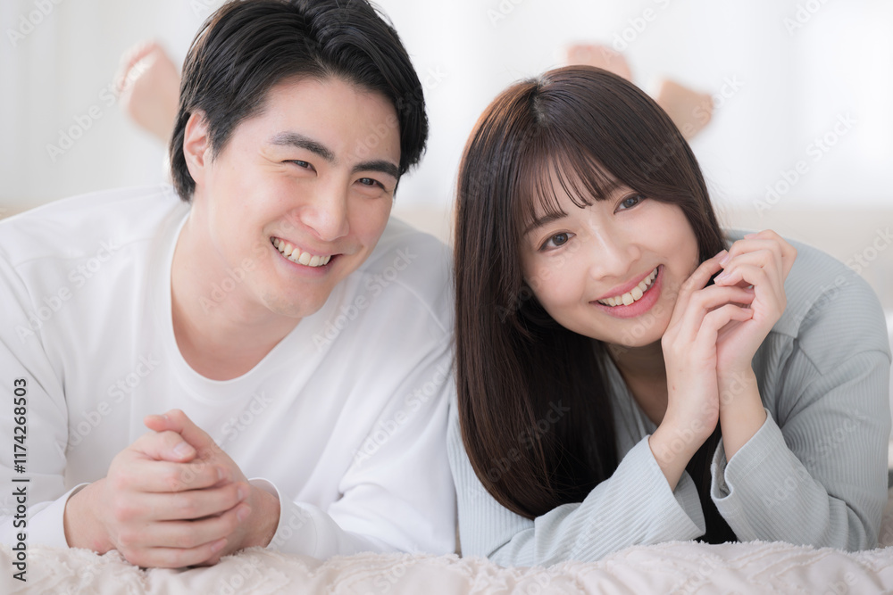 寝室のベッドで寝転んでうつ伏せで寛ぐ笑顔のカップル