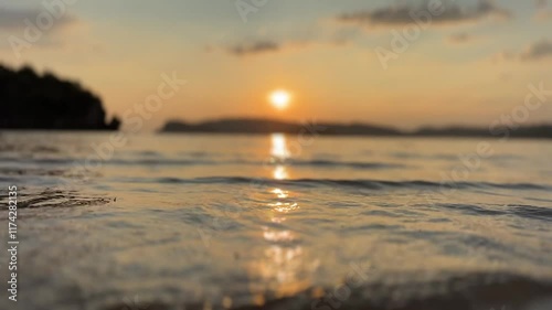 Golden sunset reflecting on calm ocean waves with a blurred shoreline and distant islands, creating a serene coastal scene. some camera shake.
