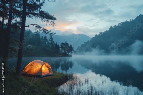 Orange camping tent by a lake surrounded by misty mountains at sunrise photo