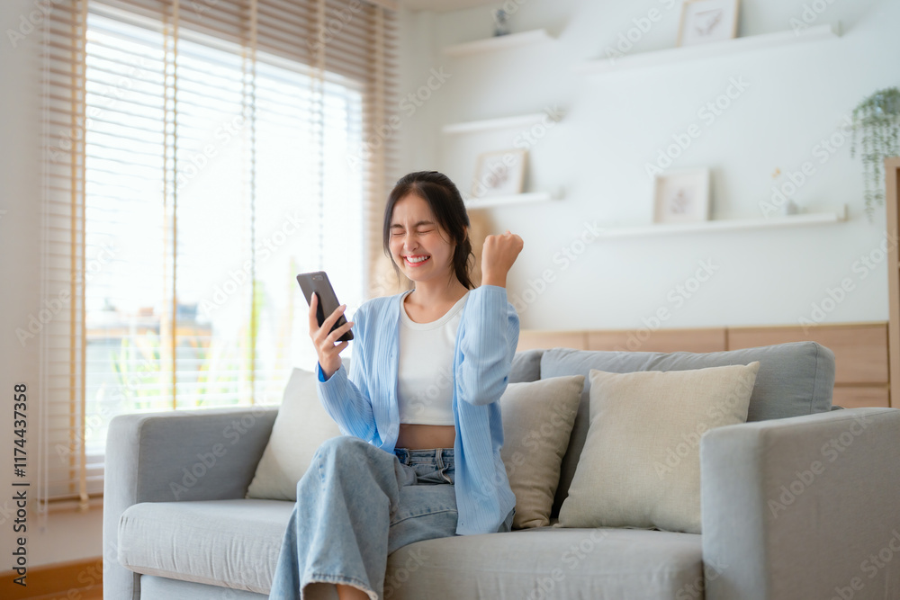 Smiling pretty young Asian woman sitting on cozy couch, using funny mobile apps in living room. Woman at Home, Doing Online Shopping, Messaging Friends, Posting on Social Media Smiling pretty young Asian woman sitting on cozy couch, using funny mobile apps in living room. Woman at Home, Doing Online Shopping, Messaging Friends, Posting on Social Media