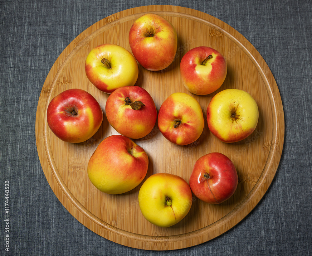 Beautiful fresh juicy red and yellow garden apples lie on a round bamboo cutting board, top view. Beautiful fresh juicy red and yellow garden apples lie on a round bamboo cutting board, top view.
