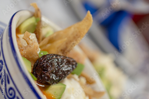 Close-up of a Mexican tortilla soup in a talavera bowl with tortilla chips, fresh avocado, and queso fresco. photo