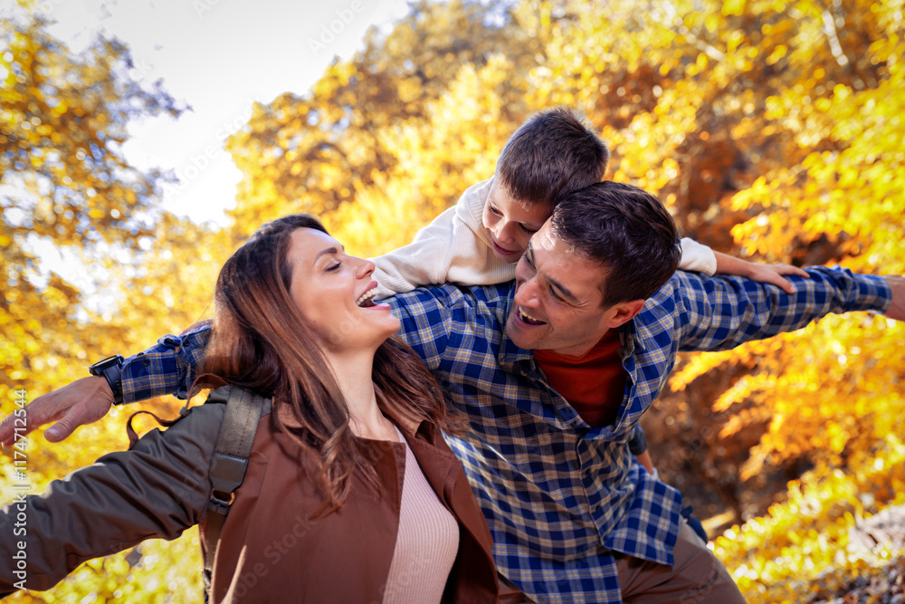 Smiling father gives his young son a piggyback ride on his back in autumn park. Mother is smiling. Family in the park. Smiling father gives his young son a piggyback ride on his back in autumn park. Mother is smiling. Family in the park.